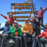 A group of hikers posing with Mount Kilimanjaro sign