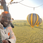 A smiling guest in a hot air balloon basket during sunrise over the plains of Tanzania, with two other balloons floating nearby