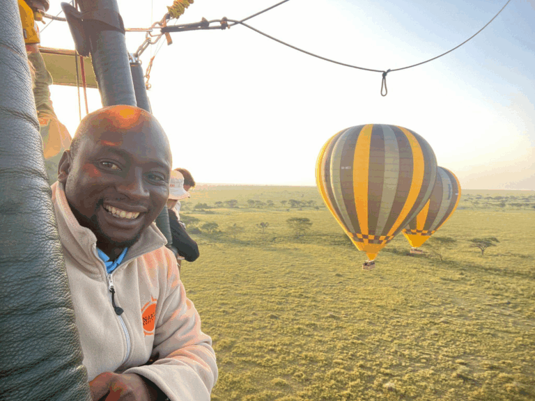 A smiling guest in a hot air balloon basket during sunrise over the plains of Tanzania, with two other balloons floating nearby